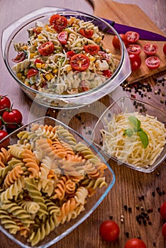 Delicious pasta salad or Mediterranean salad. Tomatoes with mozzarella basil corn spice and olive oil on a wooden table.