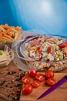 Delicious pasta salad or Mediterranean salad. Tomatoes with mozzarella basil corn spice and olive oil on a wooden table.