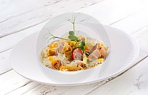 Pasta with salmon, zucchini and tomatoes in a creamy sauce on white wood background