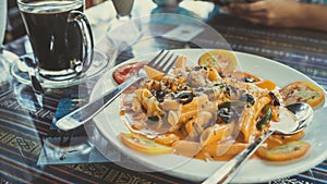 Delicious pasta with tomato sauce. Silverware placed on plate of palatable pasta with tomato sauce and olives on