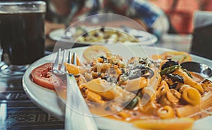 Delicious pasta with tomato sauce. Silverware placed on plate of palatable pasta with tomato sauce and olives on