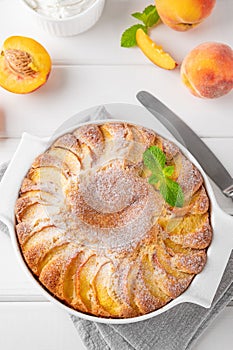 Delicious peach pie in a white ceramic baking form on a white wooden background. Summer cake. Selective focus, copy space