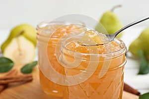 Delicious pear jam and spoon on blurred background, closeup