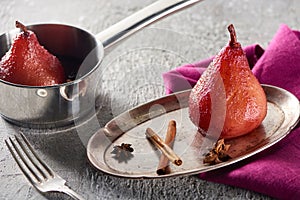 Delicious pear in wine with cinnamon and anise on silver plate and in stewpot on grey concrete surface with pink napkin and fork