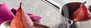 Delicious pear in wine on silver plate and in stewpot on grey concrete surface with pink napkin, panoramic shot