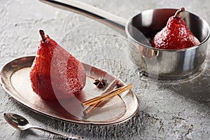 Delicious pear in wine in stewpan and on silver plate with cinnamon and anise on grey concrete surface
