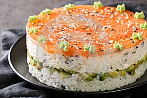 Delicious philadelphia sushi cake with red fish, rice, avocado, cream cheese, seaweed, sesame seeds decorated with wasabi close-up