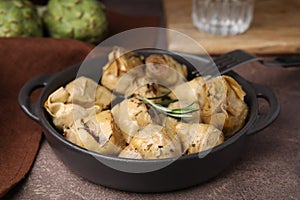 Delicious pickled artichokes with rosemary served on brown table, closeup