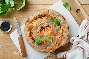 Delicious pie Spanakopita with soft feta cheese and spinach on old light wooden table backgrounds. Traditional Greek Spiral filo