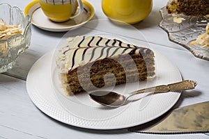 Delicious piece of cake with cream  nuts and chocolate close-up on a white plate  coffee in a yellow cup on a light wooden table