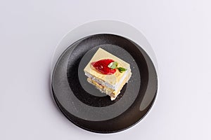 Delicious piece of white Shortcake on a black plate, decorated with fresh red strawberries