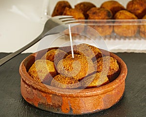 Delicious pincho of several round croquettes in a bowl of mud on a black slate board decorated with croquettes in a plastic box