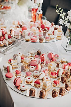 Delicious pink candy bar at wedding reception. Pink and white desserts,macarons and cupcakes on stand, modern sweet table at