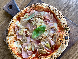Delicious pizza Capriciosa consisting of tomatoes, Mozzarella cheese, ham, marinated mushrooms, artichoke, basil and butter. Pizza