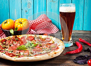 Delicious pizza, glass of beer vegetables and spices on wooden table