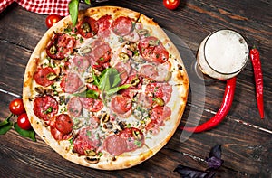 Delicious pizza, glass of beer vegetables and spices on wooden table.