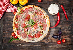 Delicious pizza, glass of beer vegetables and spices on wooden table.