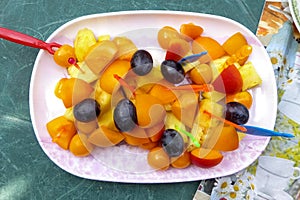 Delicious plate with fruit salad consisting of grapes , apples , peaches , pineapple and physalis . Barbecue with vitamin bar .
