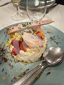 delicious plate with russian salad, red peppers, corn and a piece of tuna belly on top in a plate decorated with edible flowers