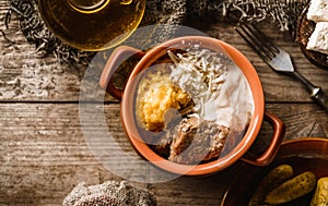 Delicious polenta with meat, cheese and sour cream in bowl on rustic wooden background. Traditional Romanian food, top view