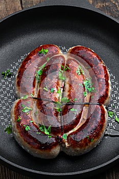 Delicious pork chipolatas sausages in a frying pan on wooden background
