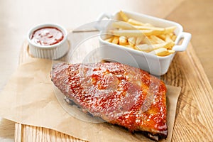 Delicious Pork ribs. Full rack of ribs BBQ on wooden plate with french fries and salad
