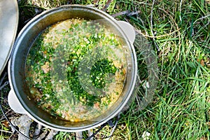 Delicious porridge cous cous with meat, vegetables and fresh herbs in a pot cooking on the nature