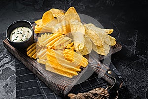 Delicious Potato chips - Crinkle, homemade, hot BBQ on a wooden board. Black background. Top view