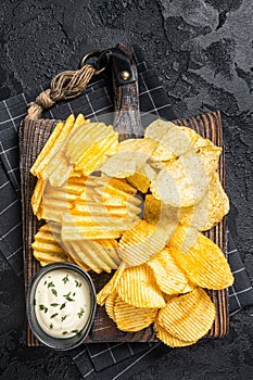 Delicious Potato chips - Crinkle, homemade, hot BBQ on a wooden board. Black background. Top view