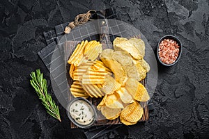Delicious Potato chips - Crinkle, homemade, hot BBQ on a wooden board. Black background. Top view
