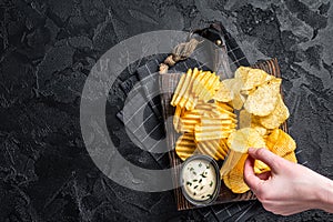 Delicious Potato chips - Crinkle, homemade, hot BBQ on a wooden board. Black background. Top view. Copy space