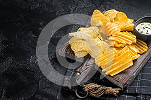Delicious Potato chips - Crinkle, homemade, hot BBQ on a wooden board. Black background. Top view. Copy space