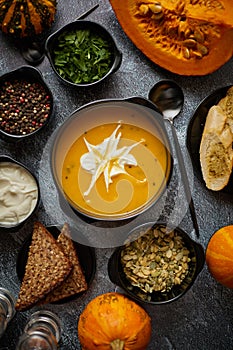 Delicious pumpkin soup with cream, seeds, bread and fresh herbs in elegant ceramic black bowl