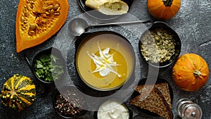 Delicious pumpkin soup with cream, seeds, bread and fresh herbs in elegant ceramic black bowl