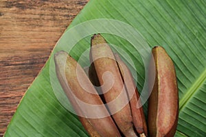 Delicious purple bananas and fresh leaf on wooden table, flat lay