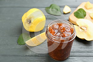 Delicious quince jam and fruits on grey wooden table. Space for text