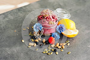 Delicious raspberry ice cream with pumpkin seeds and hempseed, decorated with blue cornflowers, black currant, sliced lemon on
