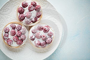 Delicious raspberry tartlets on a white vintage plate. Sweet treat on a light blue background. Flat lay and copy space. Top view
