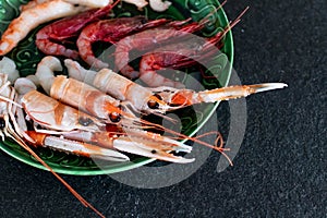 Delicious raw crustacean, luxury mix of fresh shellfish on a green plate. Prawns, scampi and fresh red prawns ready to eat raw.