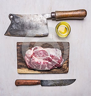 Delicious raw pork steak on a cutting board with a meat cleaver and a knife for meat on wooden rustic background top view close up