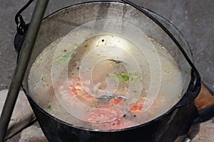 Delicious red salmon fish fresh-soup cooked in large bowler on campfire outdoors