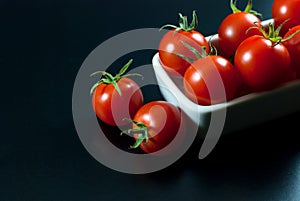 Delicious red tomatoes are housed in white ceramic vessels and placed on a black floor, selective focus
