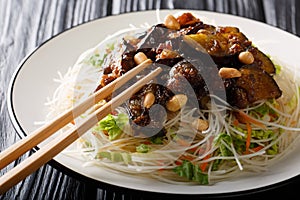Delicious rice vermicelli with caramelized eggplants and peanuts close-up on a plate. horizontal