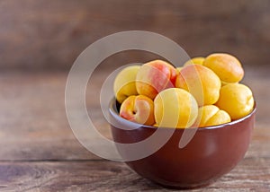 Delicious ripe apricots in a bowl on a wooden table close-up