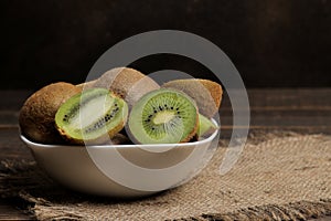 Delicious ripe many kiwi fruit and kiwi sectioned in a bowl on a brown wooden table. space for text