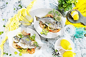 Delicious roasted dorado or sea bream fish with lemon and fresh Prawns , fresh parsley and spinach on white platter .