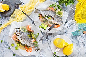 Delicious roasted dorado or sea bream fish with lemon and fresh Prawns , fresh parsley and spinach on white platter .