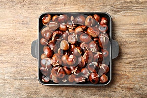 Delicious roasted edible chestnuts in baking dish on wooden table, top view