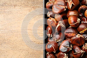 Delicious roasted edible chestnuts in baking dish on wooden table, top view. Space for text