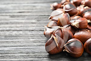 Delicious roasted edible chestnuts on black wooden table, closeup. Space for text
